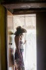 Donna in cappello solare guardando attraverso la tenda della porta — Foto stock