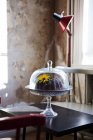 Chocolate cake in glass cakestand on table — Stock Photo