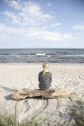 Reife Frau sitzt auf Treibholz und schaut aufs Meer — Stockfoto