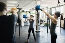Mujeres jóvenes y hombres balanceando pesas en el gimnasio - foto de stock