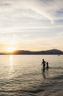 Madre e figlia guadare in mare al tramonto — Foto stock
