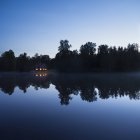 Piccola capanna con finestre illuminate sul lago di notte — Foto stock