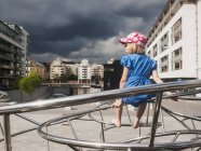 Menina sentada na instalação de metal, edifícios exteriores no fundo — Fotografia de Stock
