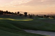 Colinas cubiertas de hierba del campo de golf en la sombra con paisaje urbano distante en el fondo - foto de stock