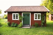 Pequena fachada de casa de campo vermelho falu com grama verde e arbustos — Fotografia de Stock