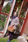 Donna anziana con cesto di mele accanto alla porta — Foto stock