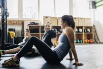 Young women and man sitting on floor in gym — Stock Photo