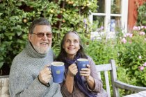 Coppia anziana bere caffè in giardino e sorridere alla fotocamera — Foto stock