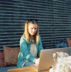 Приваблива молода жінка використовує ноутбук на літній терасі, фокус на передньому плані — стокове фото