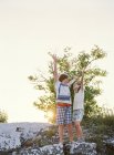 Due ragazzi in piedi sulla roccia con le mani in alto — Foto stock