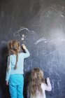 Sisters drawing on chalkboard, rear view — Stock Photo