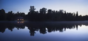 Небольшая хижина с освещенными окнами на озере ночью — стоковое фото