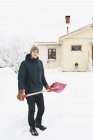Чоловік стоїть з рожевою лопатою снігу перед будинком — стокове фото