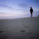 Silhouette dell'uomo in piedi sulla spiaggia sabbiosa al tramonto con impronte di primo piano — Foto stock