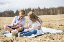 Niño y niña usando el teléfono inteligente en el prado, se centran en primer plano - foto de stock