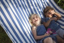 Two girls lying in striped hammock and laughing, selective focus — Stock Photo