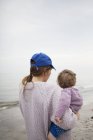 Rückansicht der Mutter, die Tochter am Strand trägt — Stockfoto
