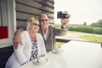 Coppia anziana seduta a tavola sul portico e scattare selfie con macchina fotografica — Foto stock