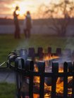 Brazier with burning wood, silhouettes of man and woman in background — Stock Photo