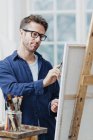 Homem usando óculos pintando no cavalete — Fotografia de Stock