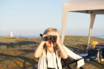 Little girl looking through binoculars at beach — Stock Photo