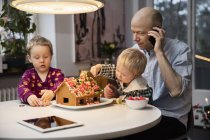 Man and two boys decorating gingerbread house — Stock Photo