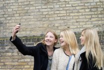 Attractive young women making selfie in front of brick wall at university campus — Stock Photo