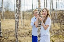Niño y niña sonriendo y mirando a la cámara en el bosque - foto de stock