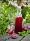Plum juice in glass and carafe, plums and stack of glasses on table — Stock Photo