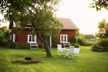 Falu casa de campo vermelha com mesa e cadeiras no gramado verde — Fotografia de Stock
