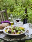 Goat cheese salad, bread, olive oil, salt, cutlery and wine on table — Stock Photo