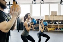 Jeunes femmes et homme cross training avec kettlebells en salle de gym — Photo de stock