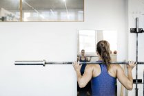 Junge Frau trainiert mit Langhantel im Fitnessstudio — Stockfoto