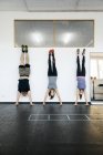 Les jeunes femmes et l'homme pratiquant handstand dans la salle de gym — Photo de stock