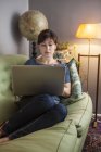 Donna con capelli castani utilizzando il computer portatile sul divano — Foto stock