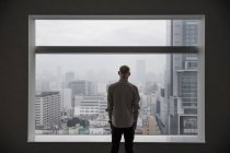 Человек смотрит на городской пейзаж через окно — стоковое фото