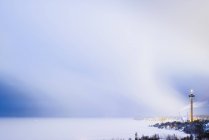 Tour de communication éclairée au-dessus de ville par lac au crépuscule — Photo de stock