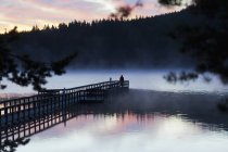 Вид на озеро и силуэт человека на пирсе на закате — стоковое фото