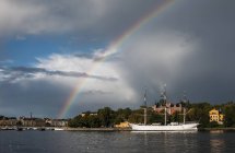 Rainbow above white sailing ship at harbor — Stock Photo