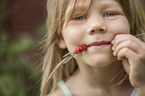 Portrait of girl with wild strawberries on spikelet in mouth — Stock Photo