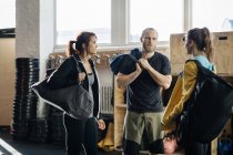 Young women and man with gym bags talking at gym, focus on foreground — Stock Photo