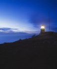 Silhouette eines Hügels mit Leuchtturm in der Abenddämmerung erleuchtet — Stockfoto