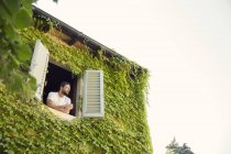 Man looking out from window of overgrown house — Stock Photo
