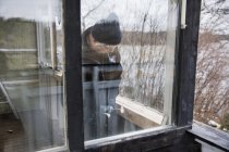 Hombre construyendo balaustrada de madera, vista desde ventana - foto de stock
