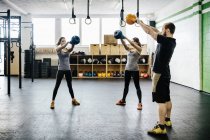 Les jeunes femmes et l'homme balançant kettlebells dans la salle de gym — Photo de stock