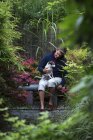 Человек, сидящий с собакой на скамейке в японском саду — стоковое фото