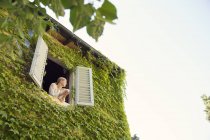 Женщина смотрит из окна заросшего дома — стоковое фото