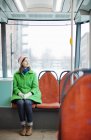 Mujer joven con abrigo verde sentada en tranvía - foto de stock