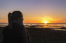 Vista panorámica de la puesta de sol sobre el mar y la mujer en primer plano - foto de stock