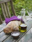 Pan casero fresco, aceite de oliva en jarra y un tazón pequeño con sal en la mesa - foto de stock